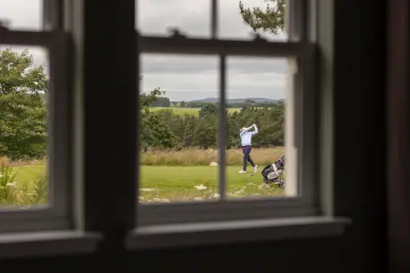 Golfer practicing swing on the golf course, seen from a window.