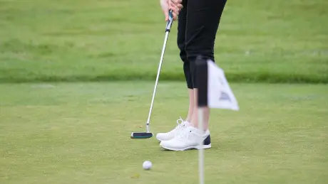 A golfer preparing to putt on the green with a golf club and ball.