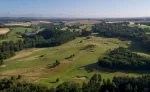 Aerial view of a lush green golf course with rolling hills and a river.