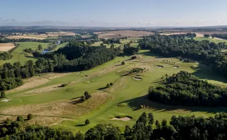 Aerial view of a lush golf course surrounded by trees and farmland.