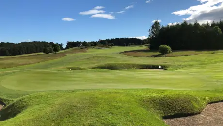 A beautiful golf course landscape with rolling hills and a flag marking the hole.