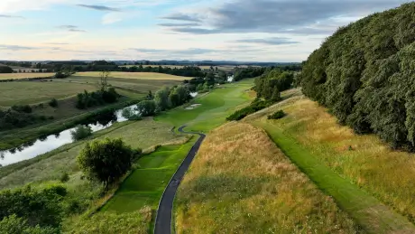 Aerial view of a stunning golf course alongside a river, surrounded by lush landscapes.