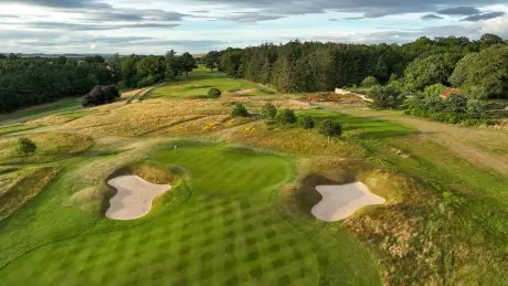 Aerial view of a lush green golf course with sand traps and trees.