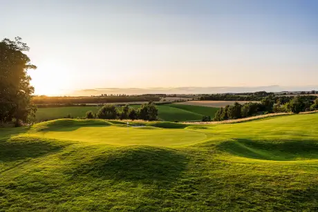 Scenic view of a lush green golf course with rolling hills at sunset.