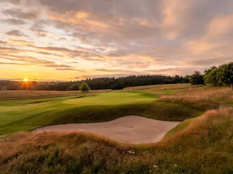 Scenic sunset at a golf course featuring a sand bunker and lush greenery.