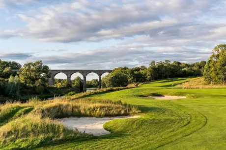 View of a stunning golf course with a stone bridge in the background.