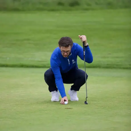 A man assessing the position of a golf ball on the green at a professional shop.