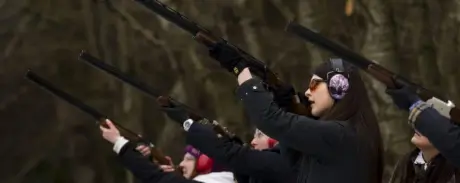 A group of individuals safely shooting shotguns at an outdoor range while wearing ear protection.